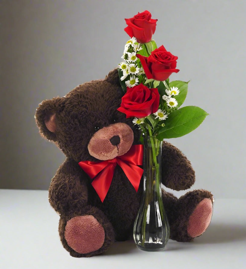 Three red rose in a bud vase with a teddy bear on the side
